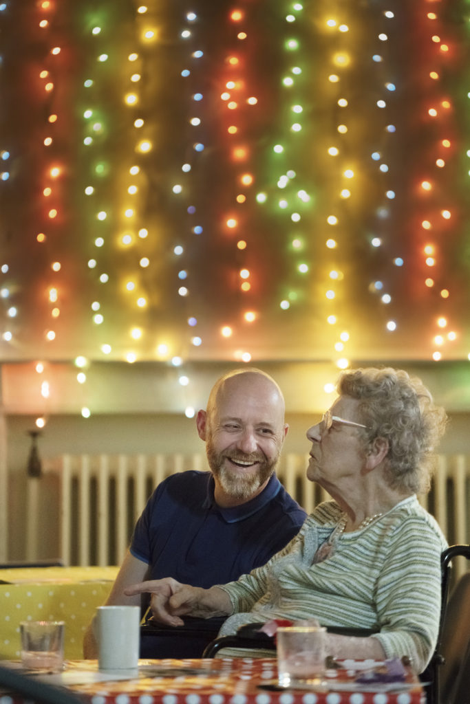 Man smiles at woman with coloured lights behind